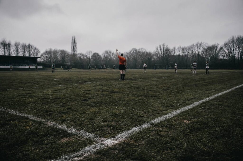Arbitre de rugby vu de loin faisant un geste bras levé sur le terrain